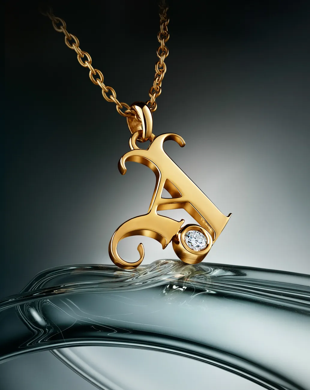 A gold initial pendant with a diamond, on rippled water · Jewellery photography, TimeLäB Studio Barcelona