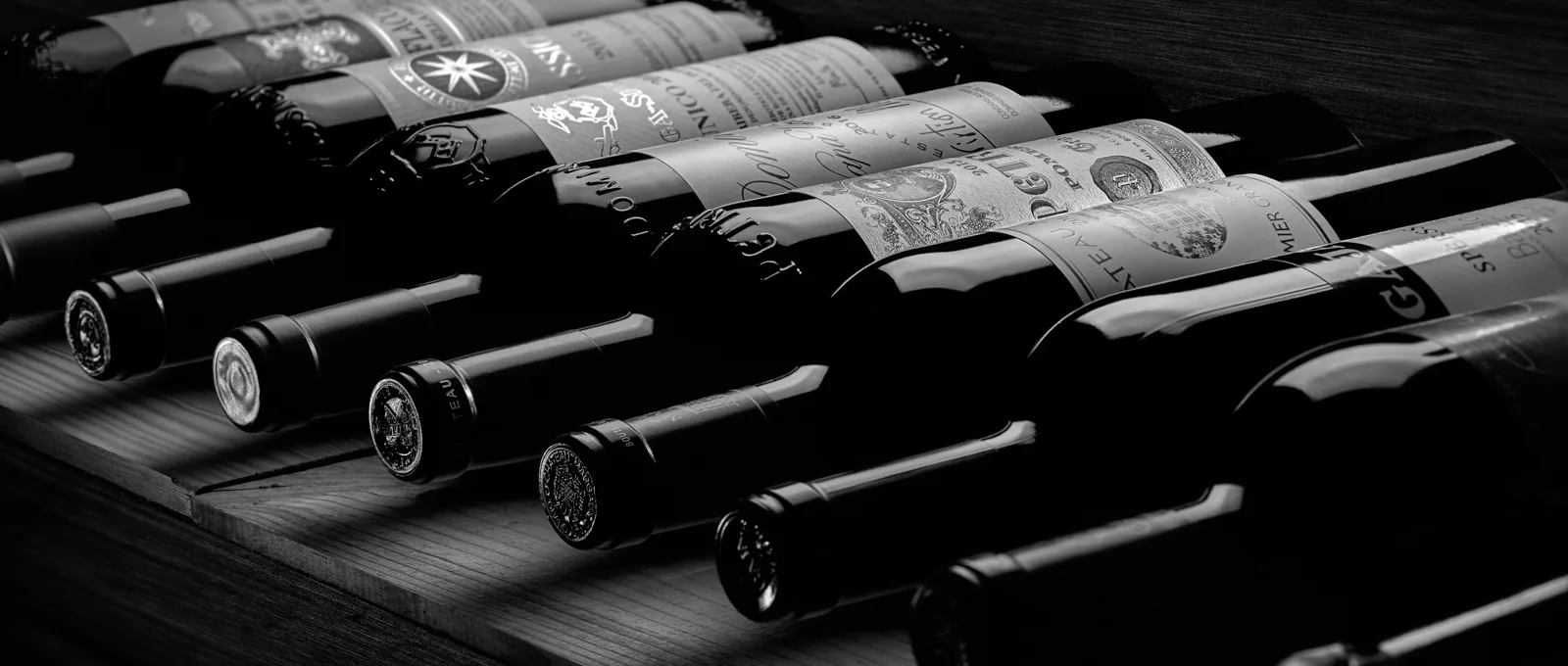 Fine wine bottles laid on their sides on a dark wooden rack, in dramatic black and white · Product photography, TimeLäB Studio Barcelona